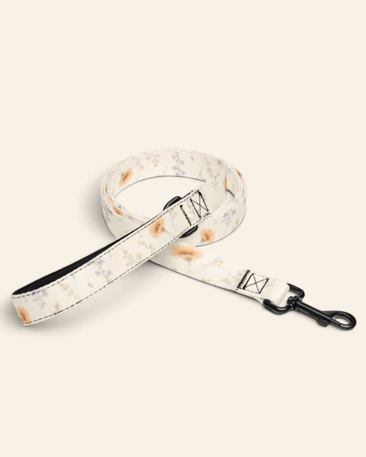 The leash coiled on a plain cream background, showing the handle loop, the adjustable slider and the black swivel snap hook. The webbing is white, printed with small apricot poppies and lilac and periwinkle wildflowers on fine stems.