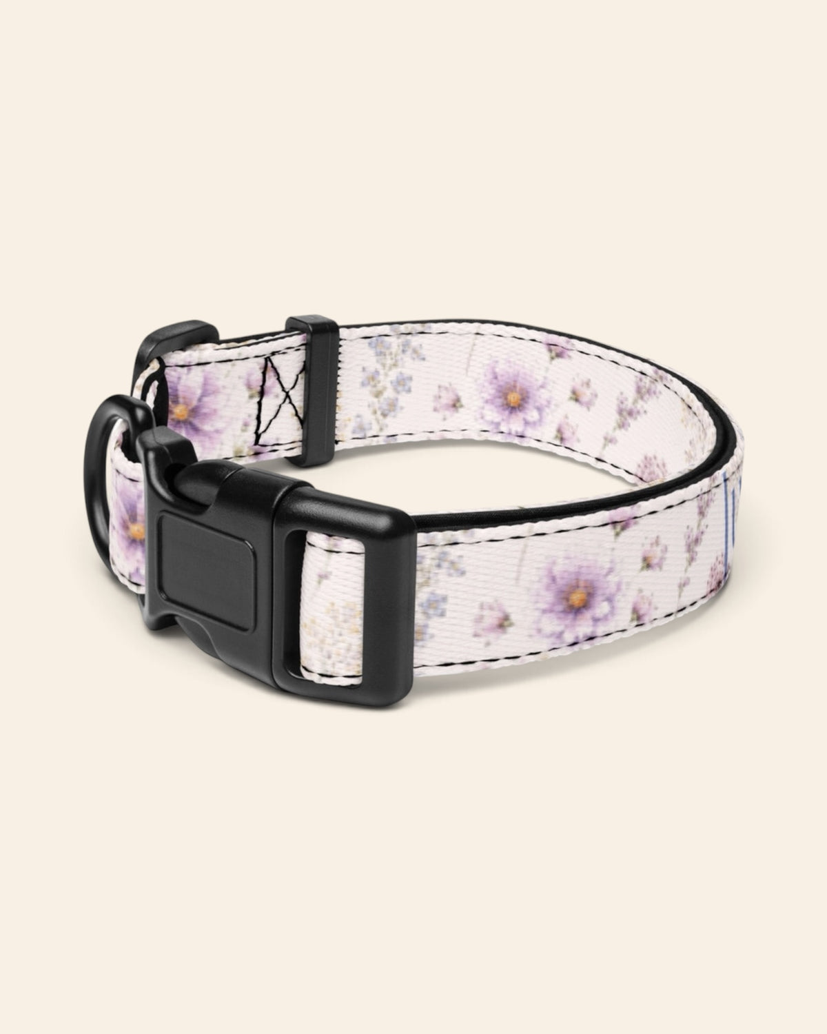 The collar alone on a plain cream background with no personalisation, stood in a ring and angled to show the black side-release buckle face, the D-ring and the tri-glide slider. The webbing is white, printed with lavender and mauve blooms on slender stems.