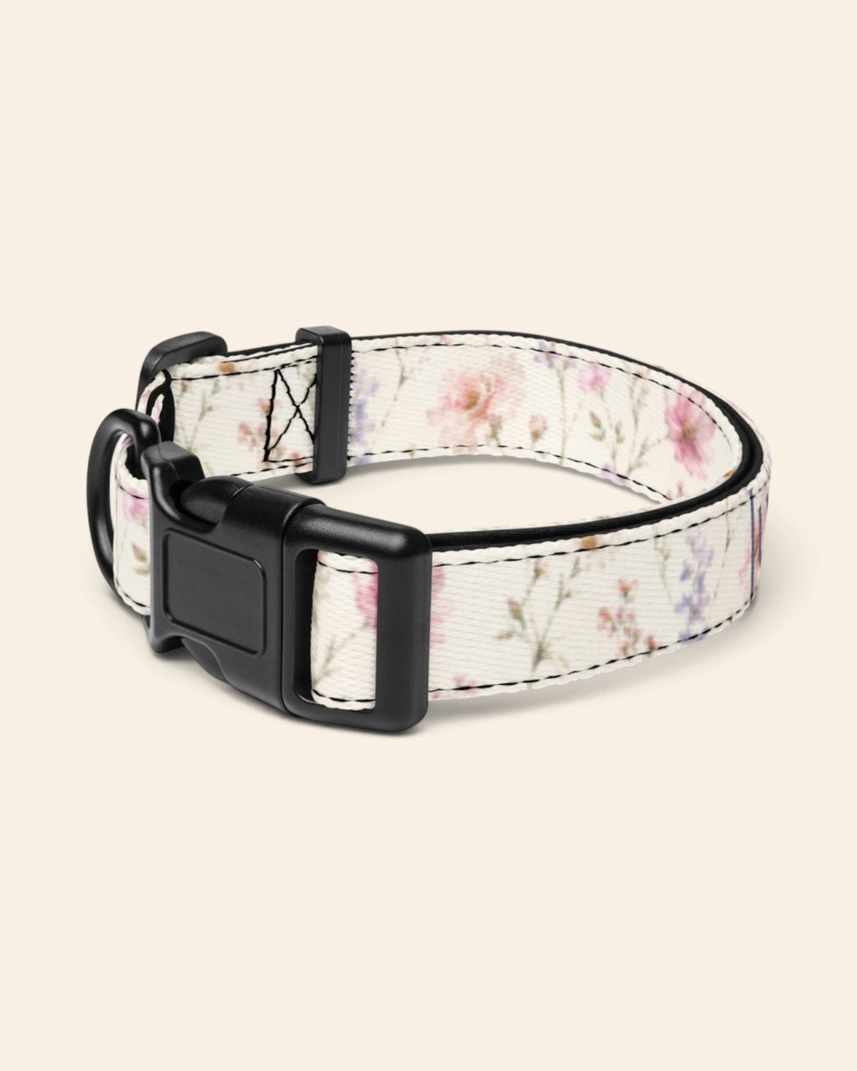 The collar alone on a plain cream background with no personalisation, stood in a ring and angled to show the black side-release buckle face, the D-ring and the tri-glide slider. The webbing is white, densely printed with pink, lilac and periwinkle wildflowers.