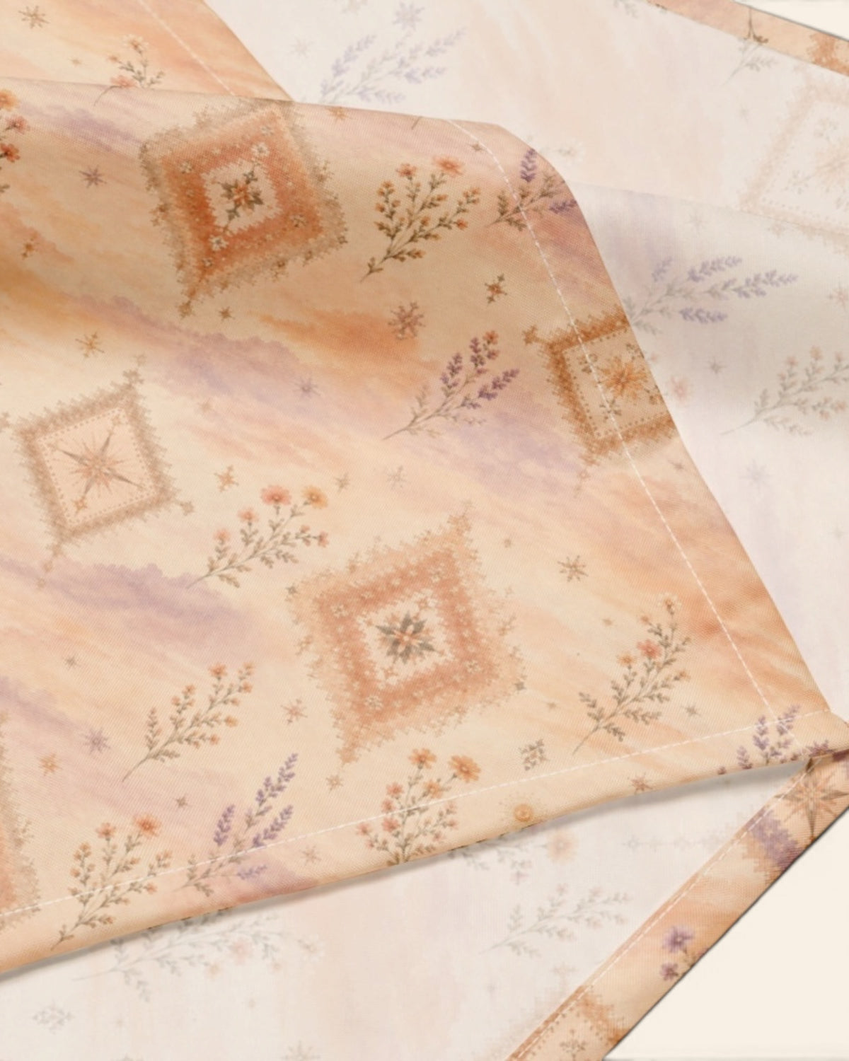 A close crop of the bandana fabric with one corner folded back over a soft cream ground, showing the print at full scale - an apricot and peach wash set with cream diamond medallions and fine sprigs.