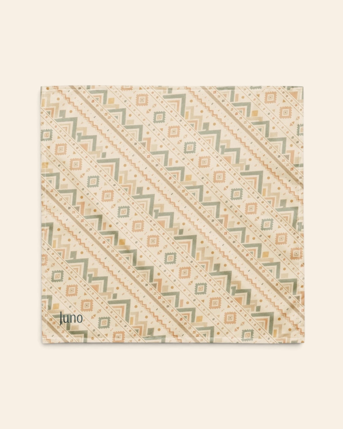 The bandana laid flat as a full square on a cream background, the print running on the diagonal. It is cream, banded with sage and apricot chevrons and diamond geometric motifs, with the sample name Juno printed in the lower left corner.
