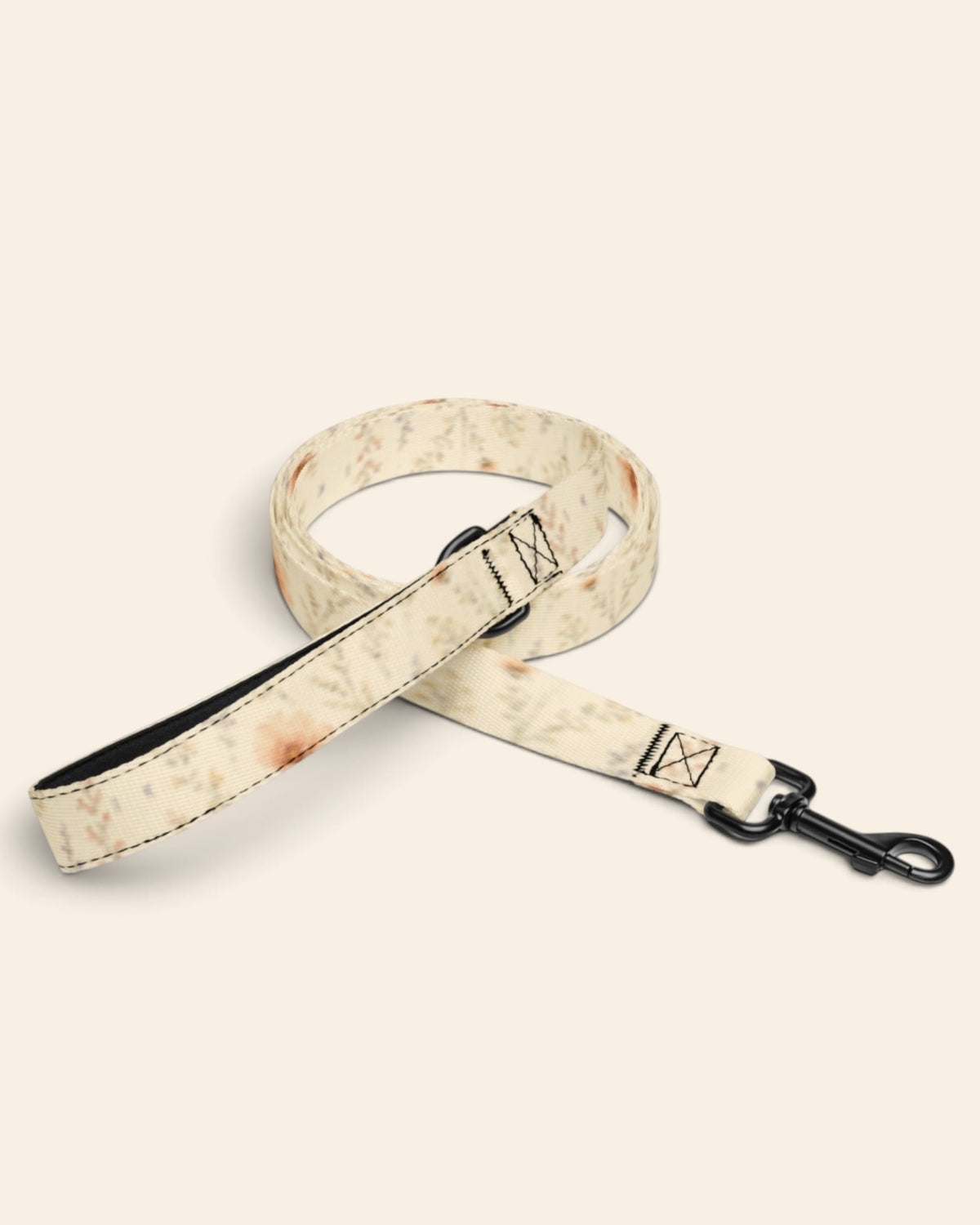 The leash coiled on a plain cream background, showing the handle loop, the adjustable slider and the black swivel snap hook. The webbing is soft butter-cream, printed with small apricot and coral blooms among fine sage stems.