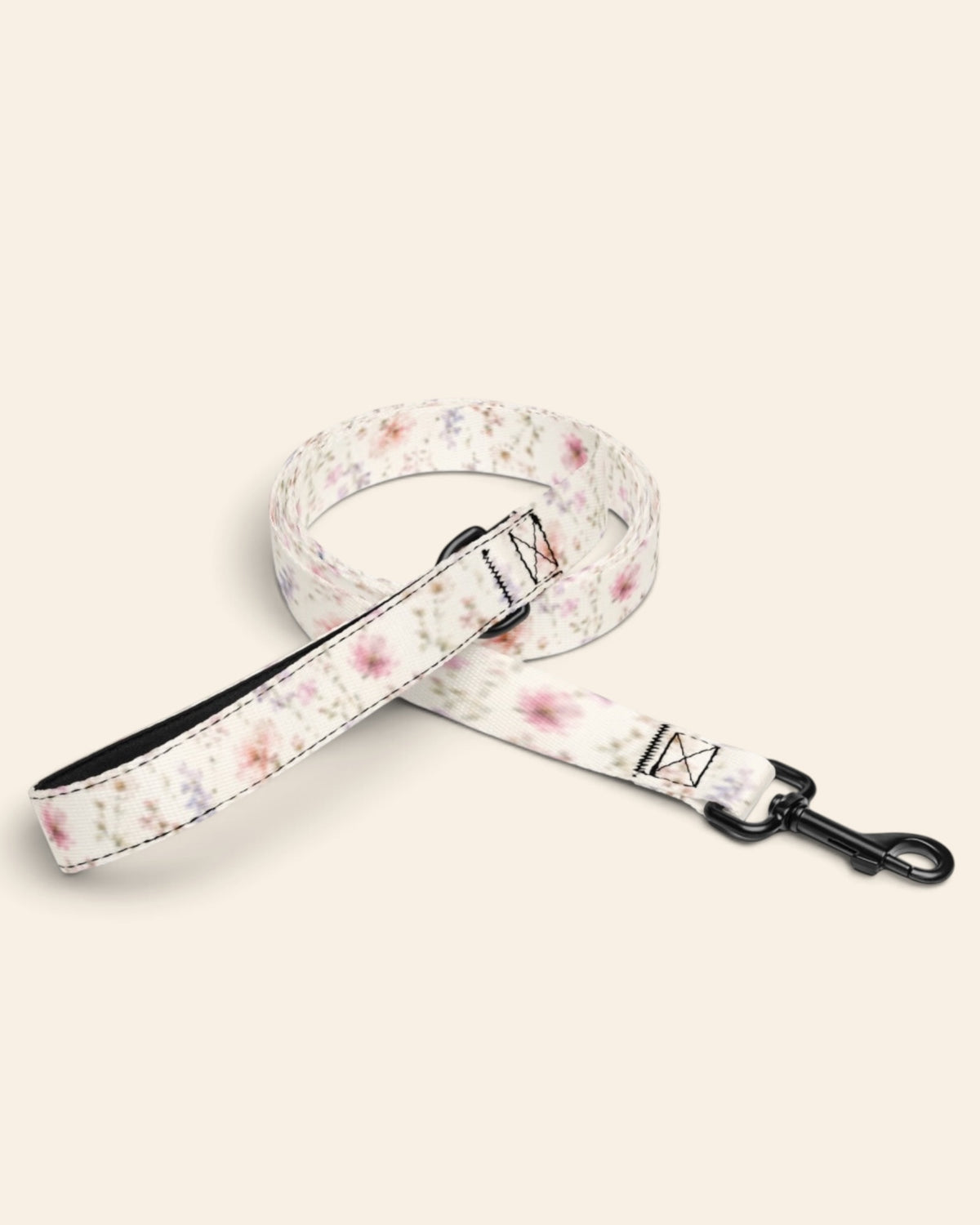 The leash coiled on a plain cream background, showing the handle loop, the adjustable slider and the black swivel snap hook. The webbing is white, densely printed with pink, lilac and periwinkle wildflowers.