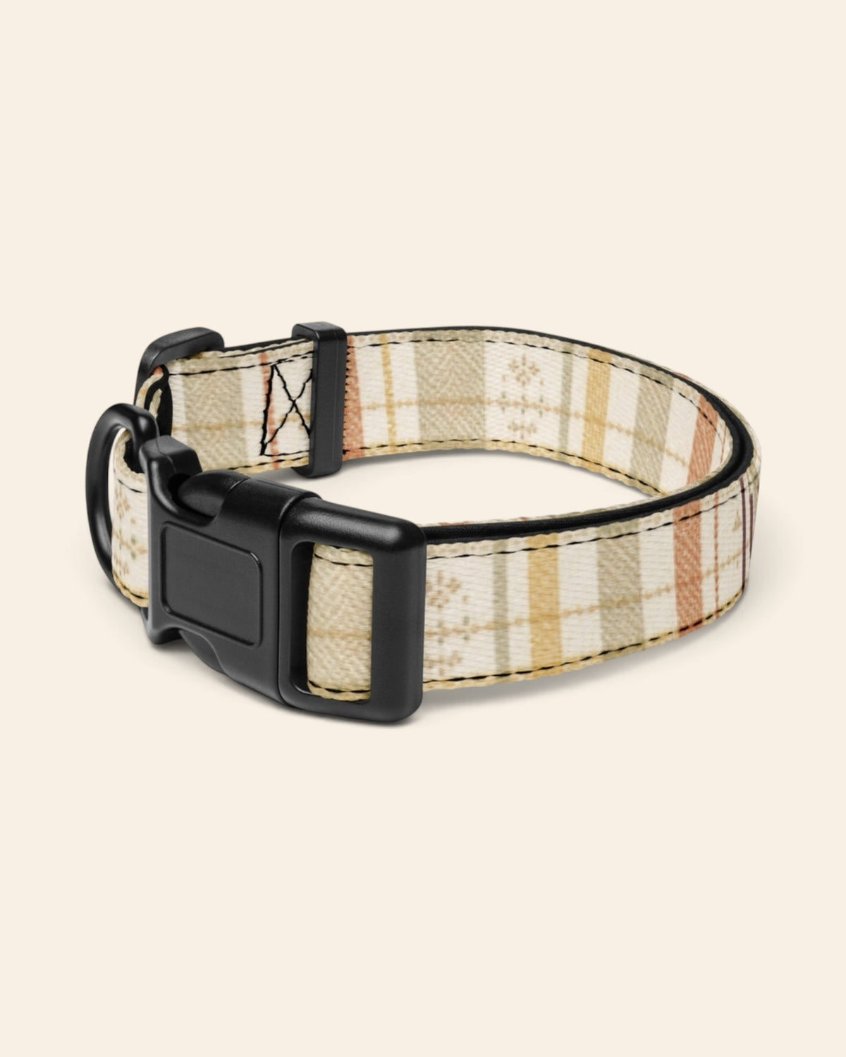 The collar alone on a plain cream background with no personalisation, stood in a ring and angled to show the black side-release buckle face, the D-ring and the tri-glide slider. The webbing is a sage, gold and apricot plaid on cream, banded with rows of small motifs.