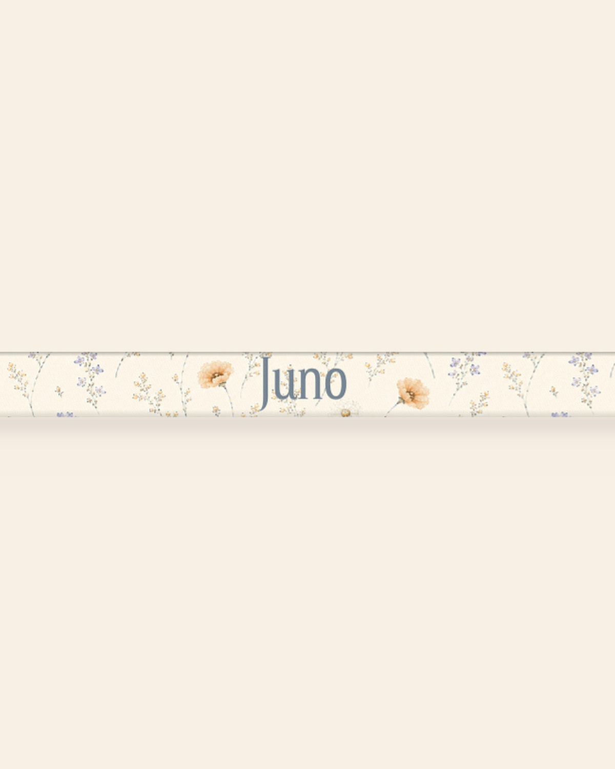 A close, straight-on crop of the leash strap laid flat on a cream background, showing the print and the sample name Juno running along the webbing. The strap is white, printed with small apricot poppies and lilac and periwinkle wildflowers on fine stems.