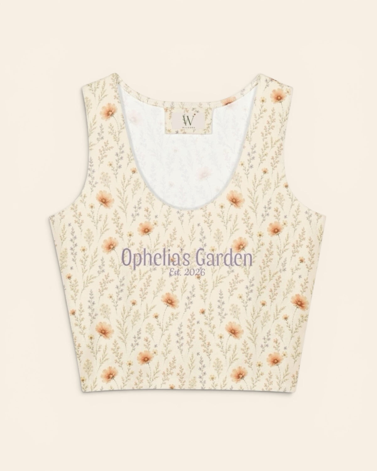 The crop tank shown from the front on a plain cream background, a scoop neck lined in white with a small woven W label at the back collar. The print is warm cream, printed with apricot cosmos blooms among fine sage stems, and the two-line caption “Ophelia’s Garden” above “Est. 2026” is printed in a small script across the chest.