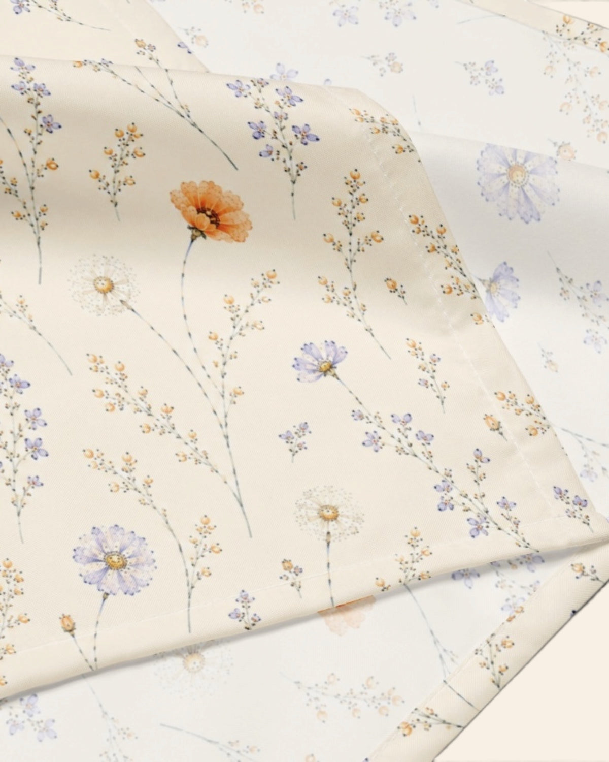 A close crop of the bandana fabric with one corner folded back over a soft cream ground, showing the print at full scale - white, printed with small apricot poppies and lilac and periwinkle wildflowers on fine stems.