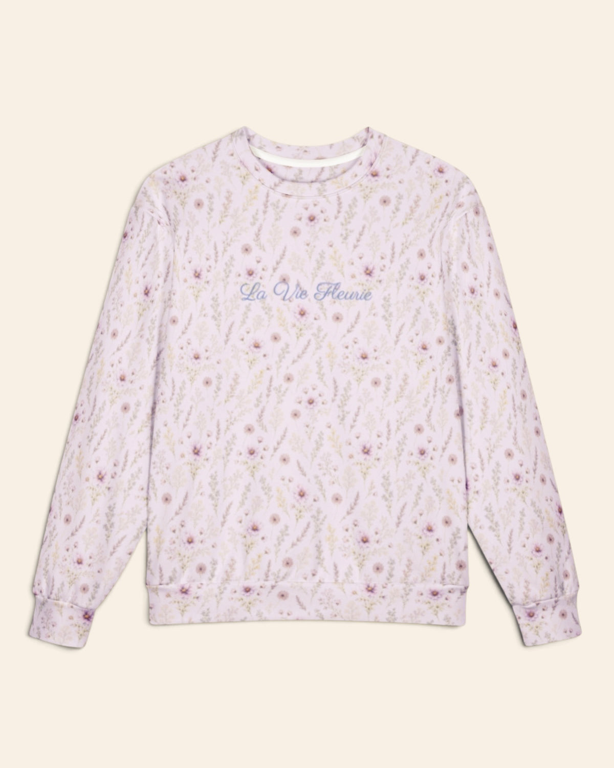 The oversized crewneck sweatshirt shown flat from the front on a plain cream background, sleeves out, cuffs and waistband ribbed. The all-over print is white, printed with lavender and mauve wildflowers on slender stems, with the words La Vie Fleurie in a small script across the chest.