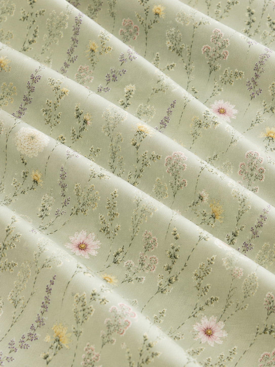A close crop of the printed fabric falling in soft diagonal folds, showing the design at full scale - sage green, printed with white and pink daisies and fine wildflower stems.