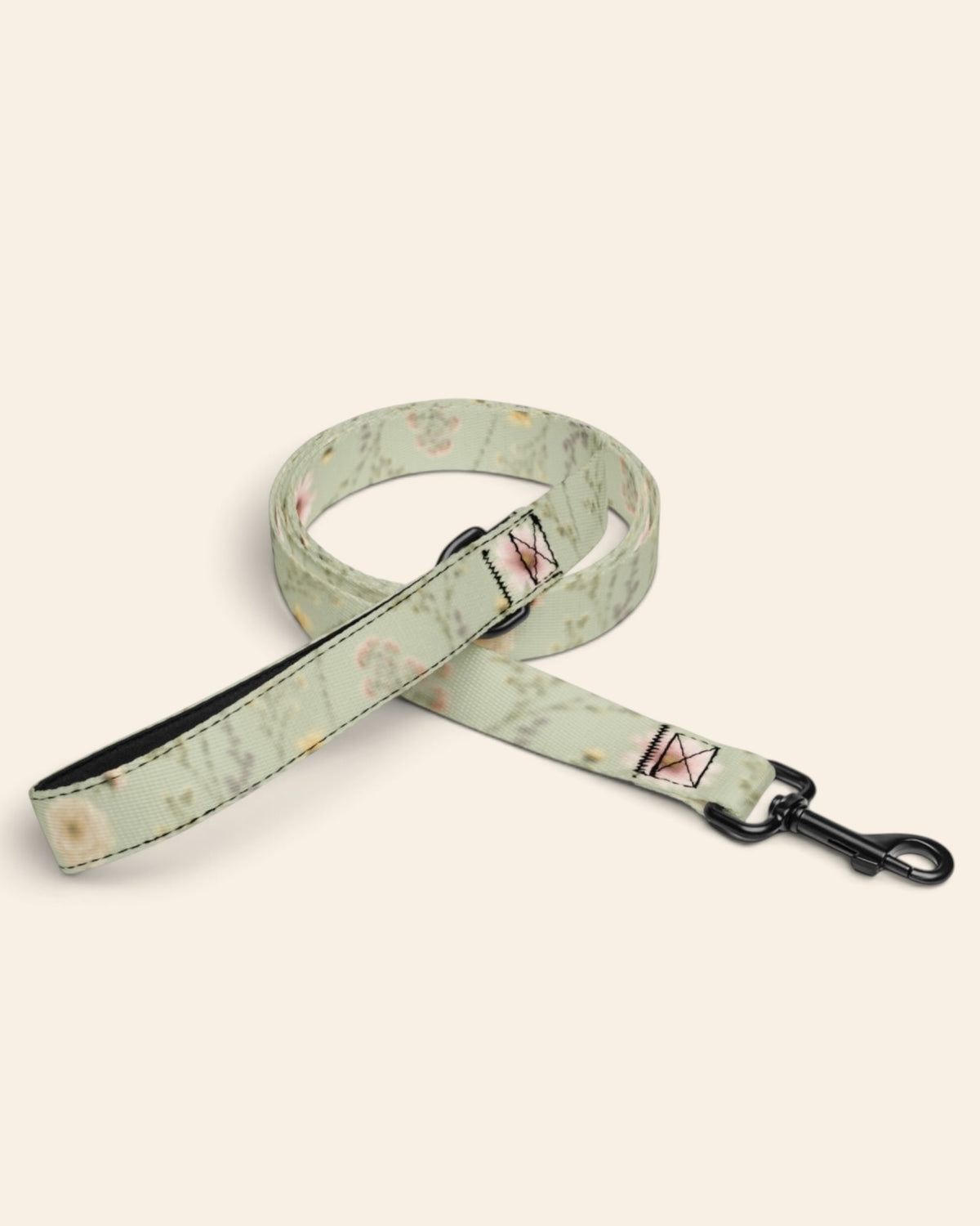 The leash coiled on a plain cream background, showing the handle loop, the adjustable slider and the black swivel snap hook. The webbing is sage green, printed with small white, pink and yellow blooms on fine stems.