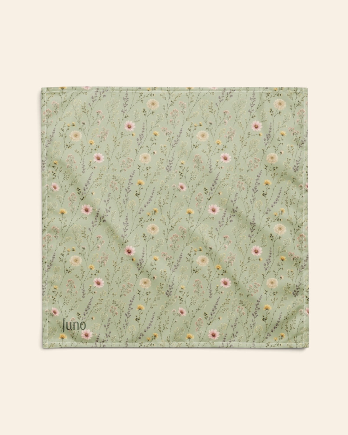 The bandana laid flat as a full square on a cream background, the print running on the diagonal. It is sage green, printed with small white, pink and yellow blooms on fine stems, with the sample name Juno printed in the lower left corner.