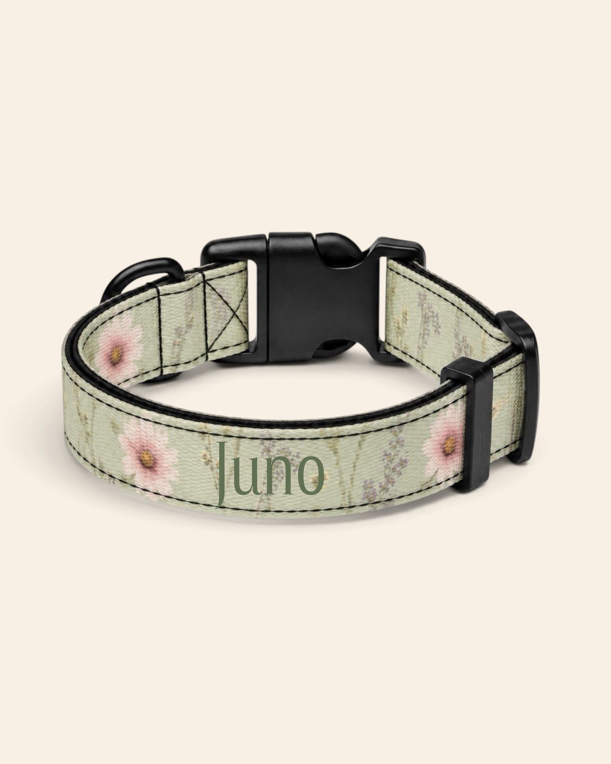 The collar alone on a plain cream background, lying in a loose loop that shows the printed webbing, a black side-release buckle and a black slider. The strap is sage green, printed with small white, pink and yellow blooms on fine stems, with the sample name Juno printed along it.