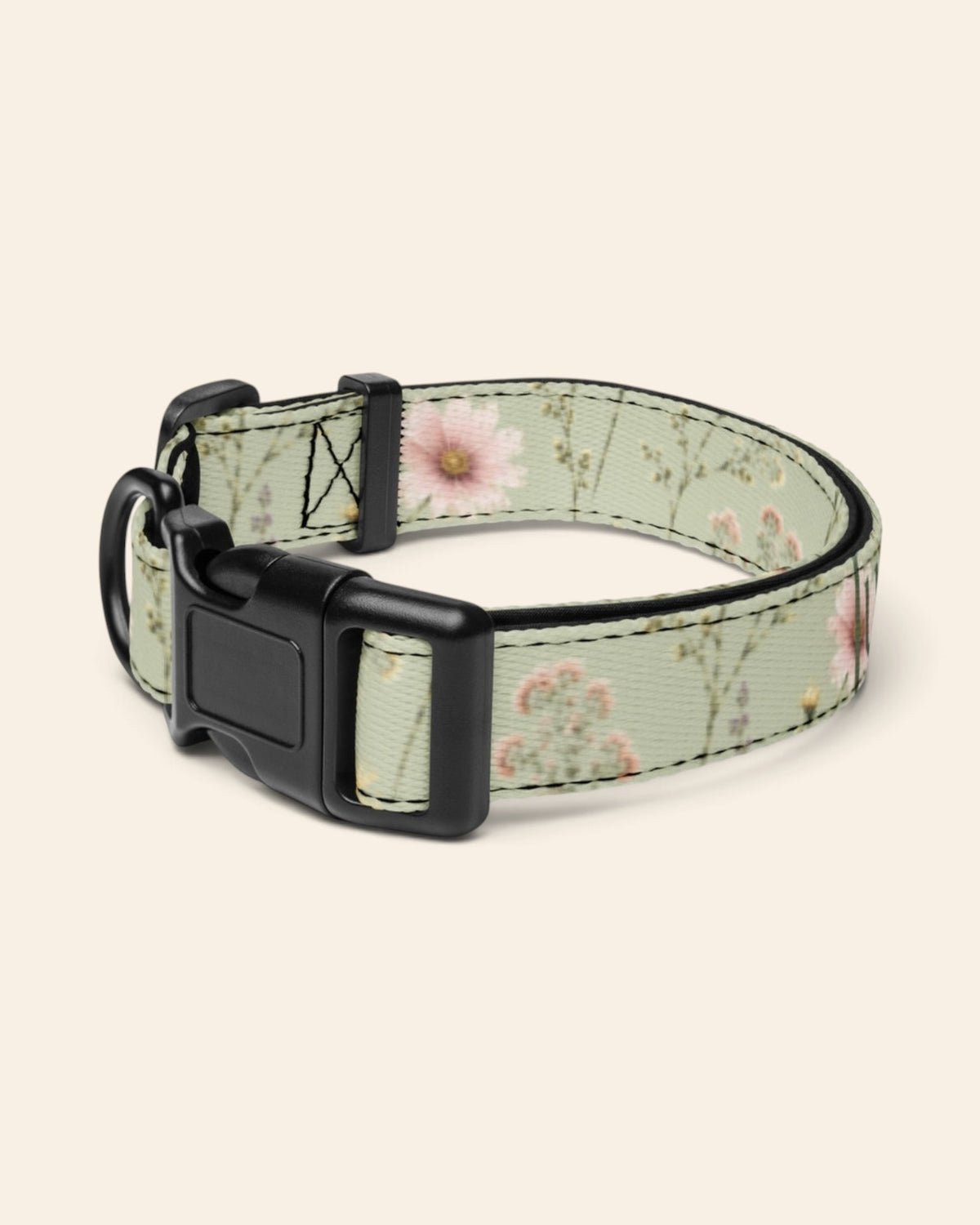 The collar alone on a plain cream background with no personalisation, stood in a ring and angled to show the black side-release buckle face, the D-ring and the tri-glide slider. The webbing is sage green, printed with small white, pink and yellow blooms on fine stems.