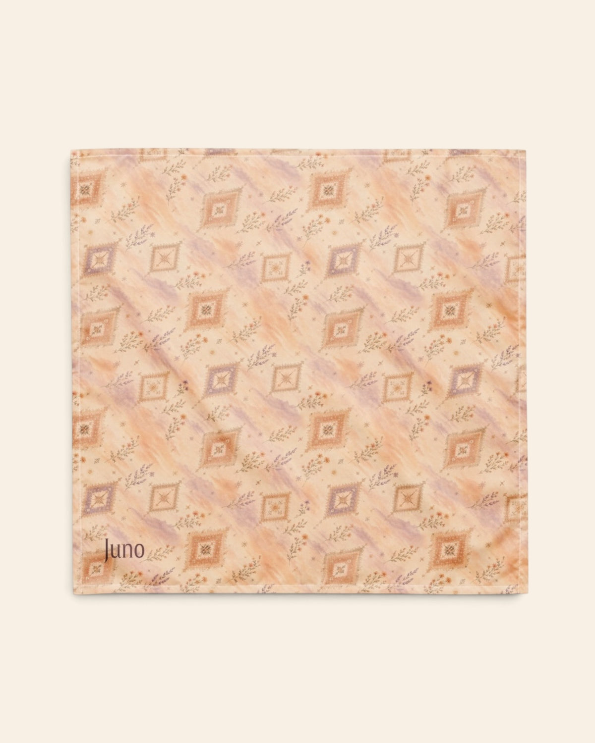 The bandana laid flat as a full square on a cream background, the print running on the diagonal. It is an apricot and peach wash set with cream diamond medallions and fine sprigs, with the sample name Juno printed in the lower left corner.