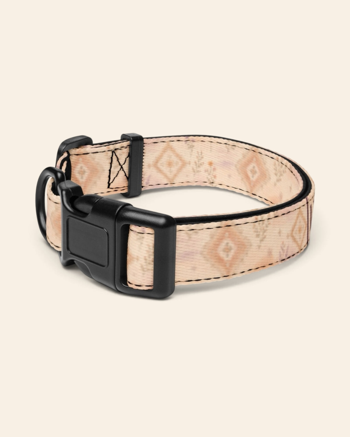 The collar alone on a plain cream background with no personalisation, stood in a ring and angled to show the black side-release buckle face, the D-ring and the tri-glide slider. The webbing is an apricot and peach wash set with cream diamond medallions and fine sprigs.