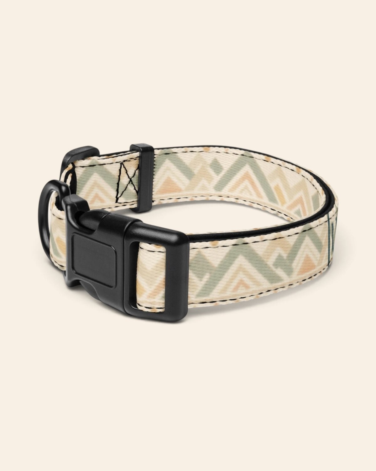 The collar alone on a plain cream background with no personalisation, stood in a ring and angled to show the black side-release buckle face, the D-ring and the tri-glide slider. The webbing is cream, banded with sage and apricot chevrons and diamond geometric motifs.
