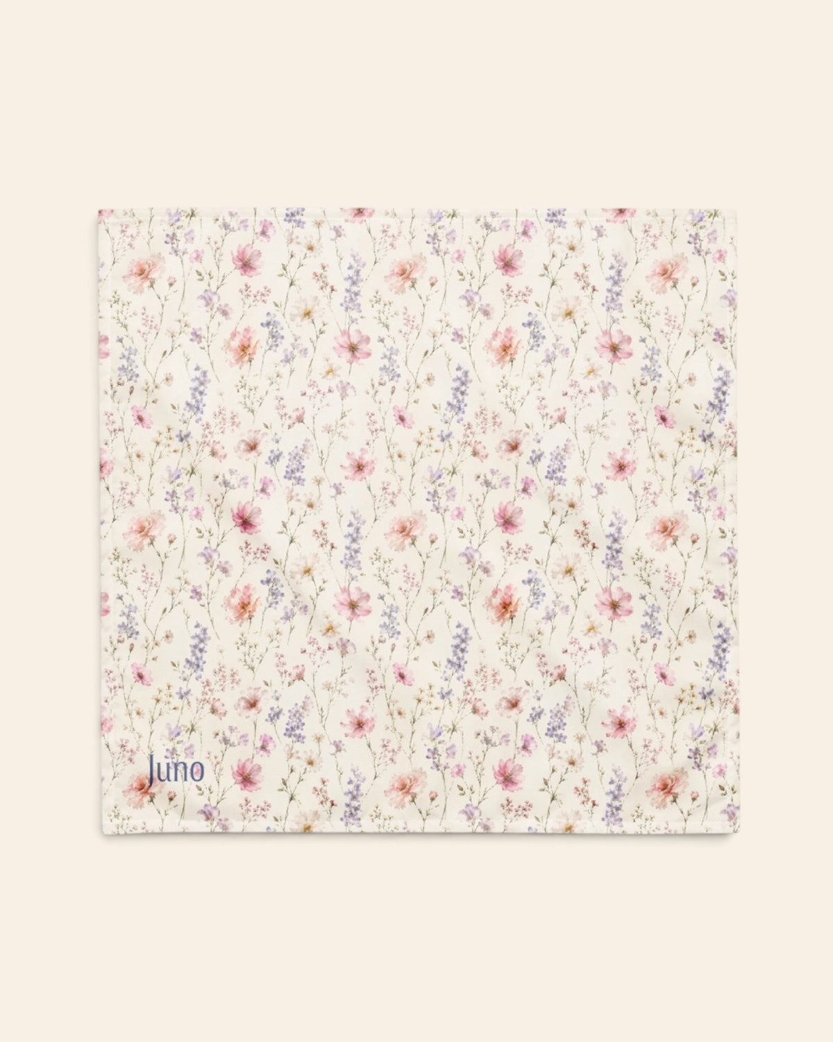 The bandana laid flat as a full square on a cream background, the print running on the diagonal. It is white, densely printed with pink, lilac and periwinkle wildflowers, with the sample name Juno printed in the lower left corner.