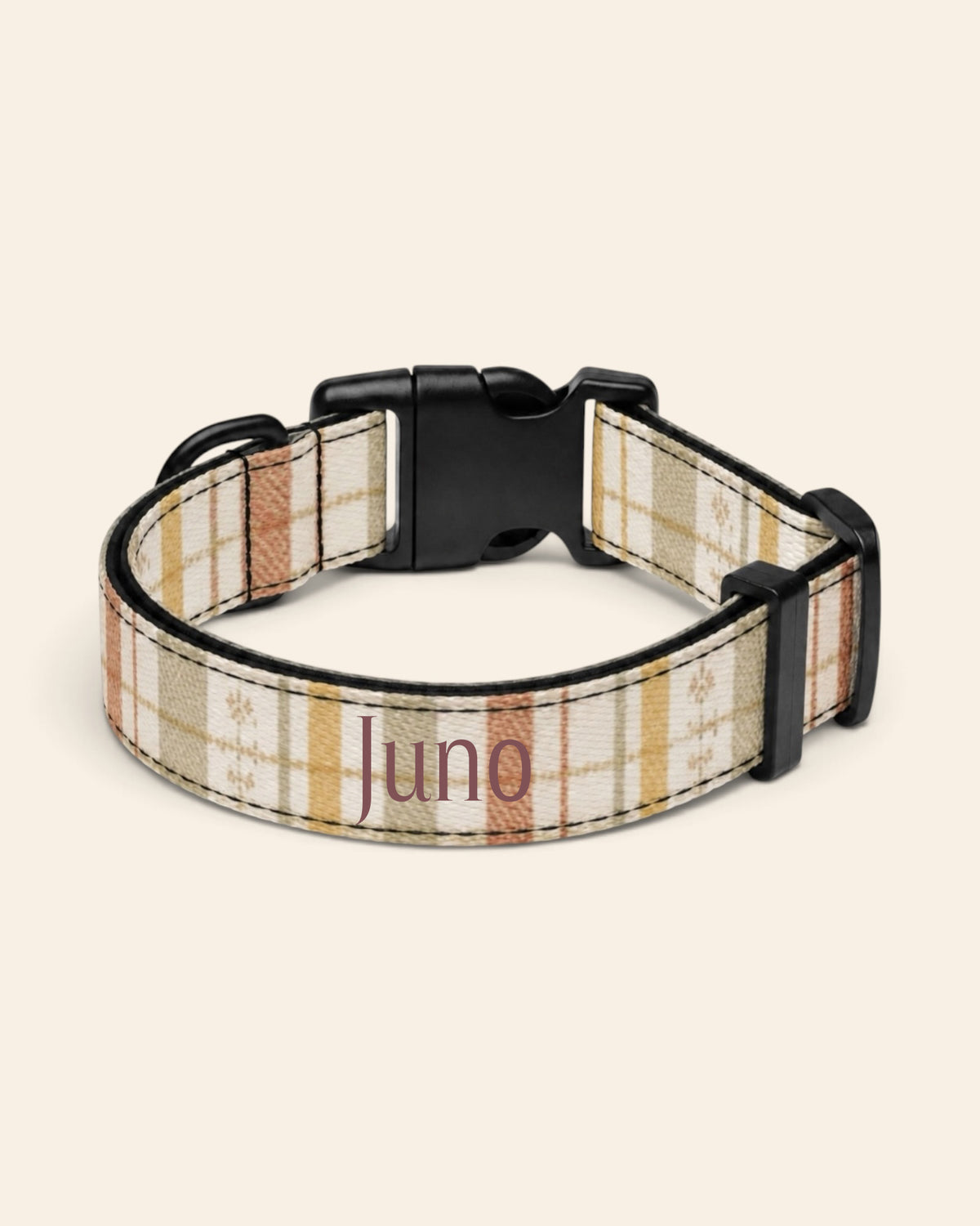 The collar alone on a plain cream background, lying in a loose loop that shows the printed webbing, a black side-release buckle and a black slider. The strap is a sage, gold and apricot plaid on cream, banded with rows of small motifs, with the sample name Juno printed along it.