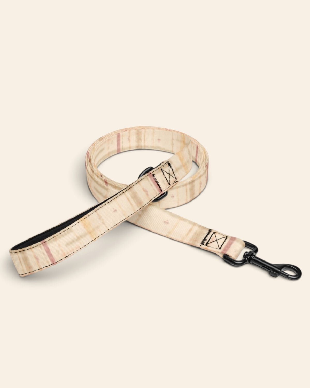 The leash coiled on a plain cream background, showing the handle loop, the adjustable slider and the black swivel snap hook. The webbing is a cream plaid crossed by apricot, rose and sage lines.