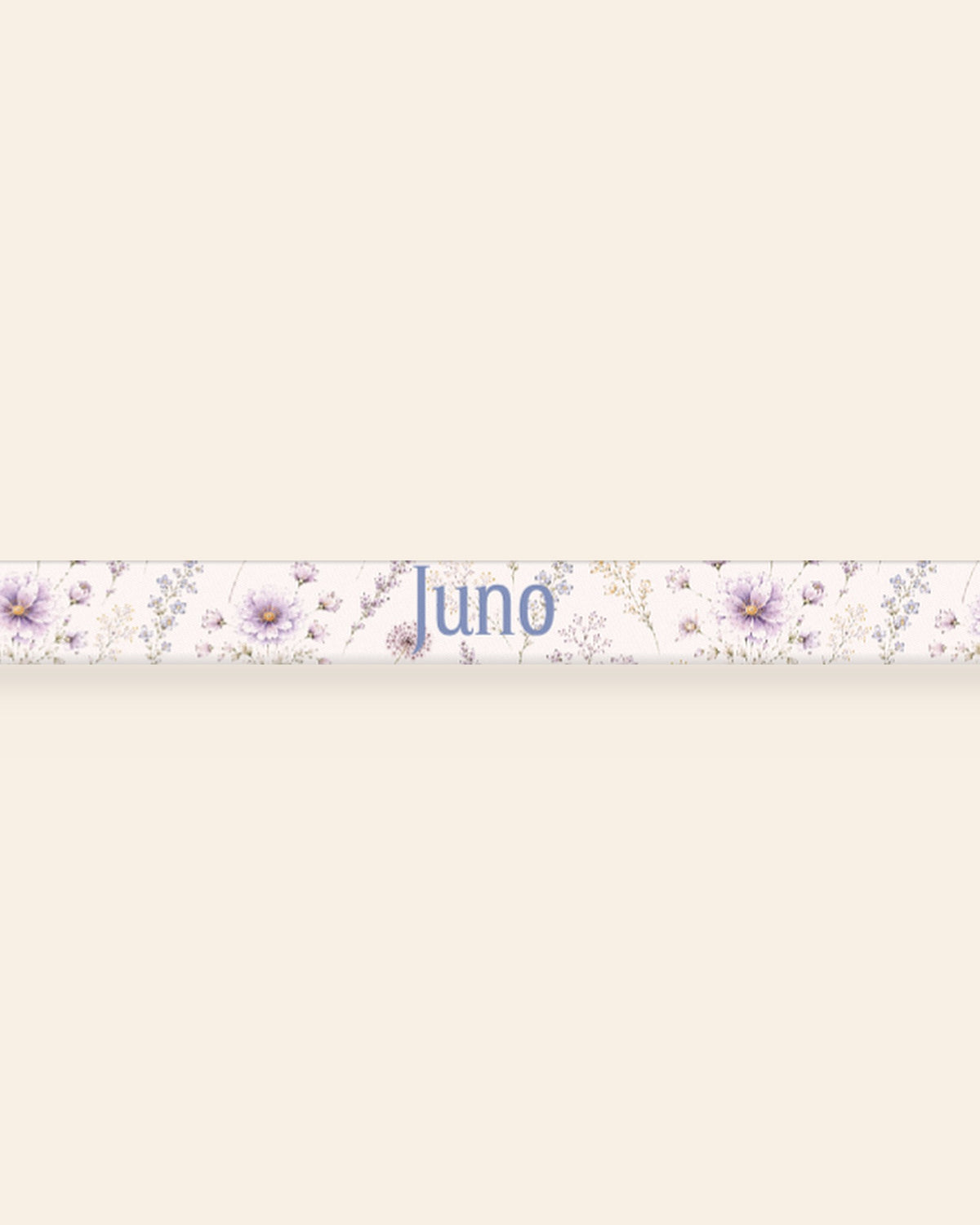 A close, straight-on crop of the leash strap laid flat on a cream background, showing the print and the sample name Juno running along the webbing. The strap is white, printed with lavender and mauve blooms on slender stems.