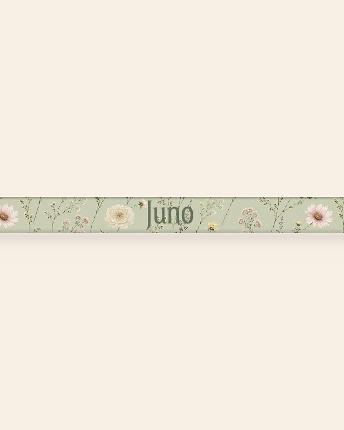 A close, straight-on crop of the leash strap laid flat on a cream background, showing the print and the sample name Juno running along the webbing. The strap is sage green, printed with small white, pink and yellow blooms on fine stems.