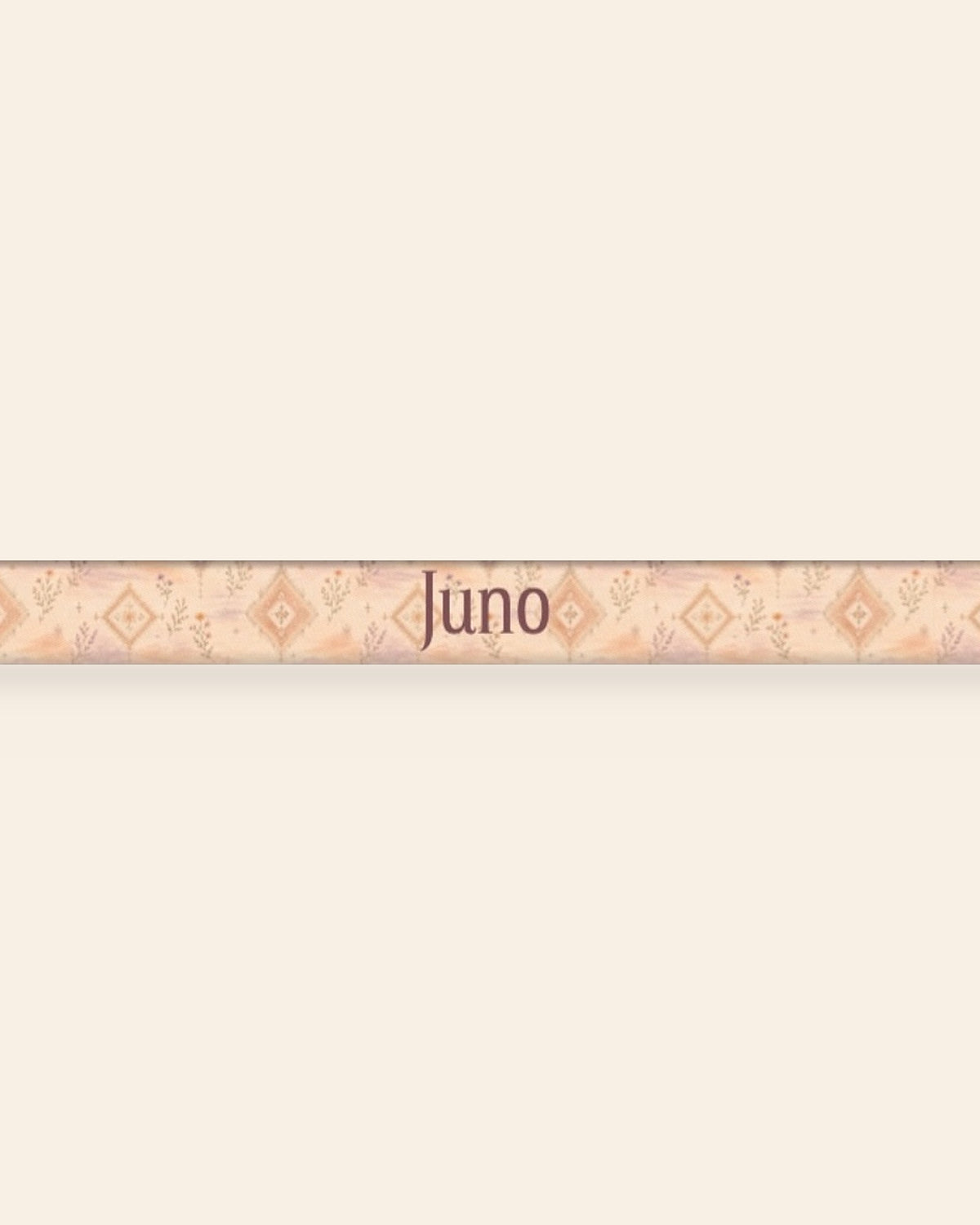 A close, straight-on crop of the leash strap laid flat on a cream background, showing the print and the sample name Juno running along the webbing. The strap is an apricot and peach wash set with cream diamond medallions and fine sprigs.