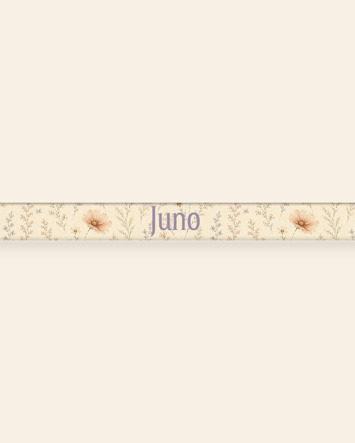 A close, straight-on crop of the leash strap laid flat on a cream background, showing the print and the sample name Juno running along the webbing. The strap is soft butter-cream, printed with small apricot and coral blooms among fine sage stems.