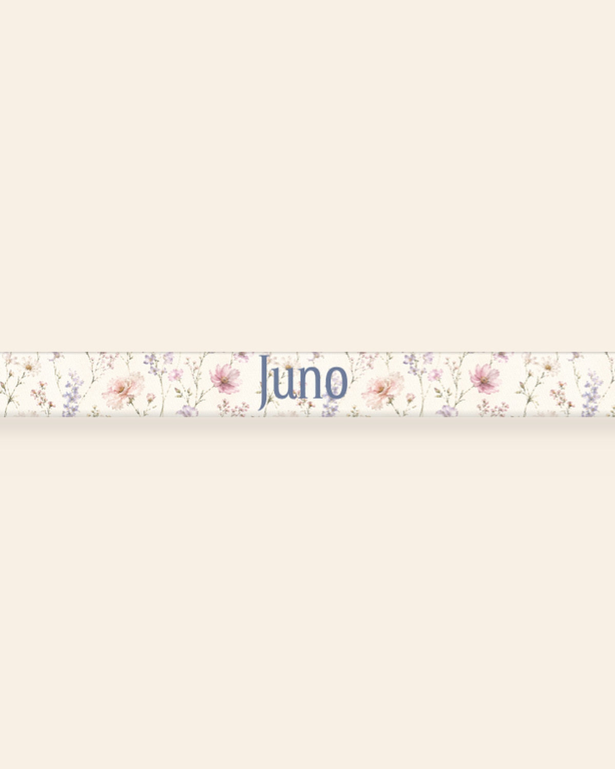 A close, straight-on crop of the leash strap laid flat on a cream background, showing the print and the sample name Juno running along the webbing. The strap is white, densely printed with pink, lilac and periwinkle wildflowers.