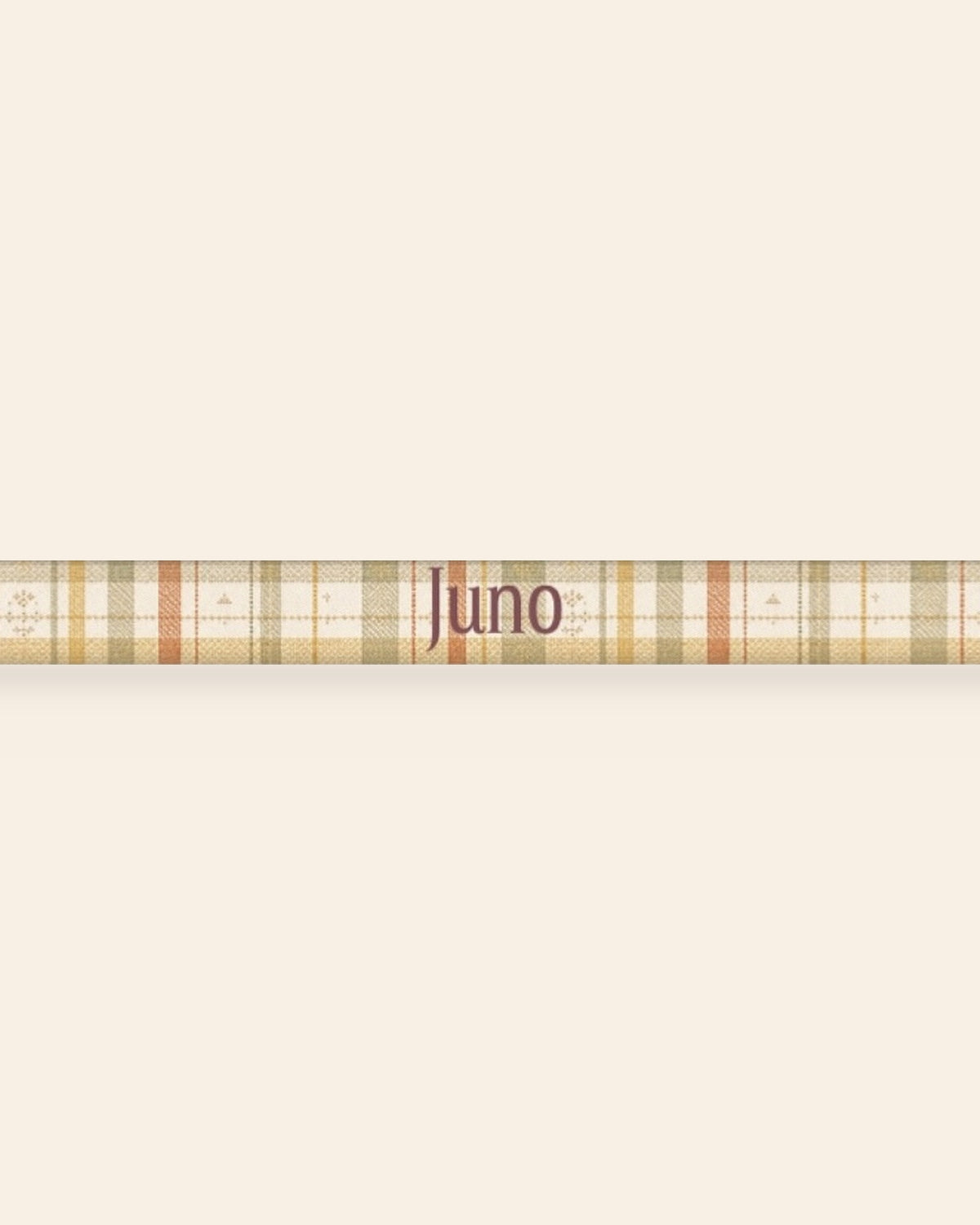A close, straight-on crop of the leash strap laid flat on a cream background, showing the print and the sample name Juno running along the webbing. The strap is a sage, gold and apricot plaid on cream, banded with rows of small motifs.